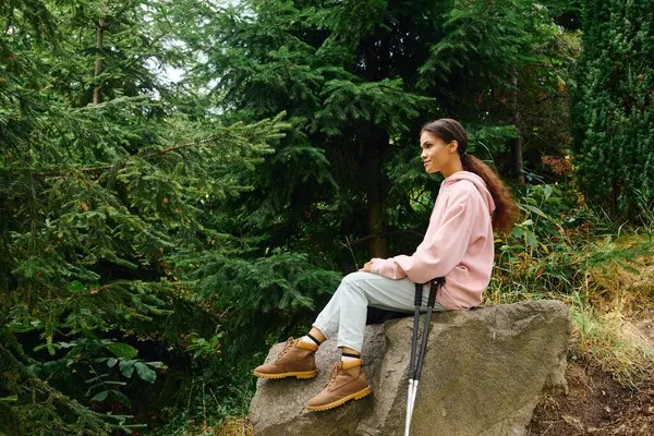 stock image Amidst the stunning autumn foliage, a young woman rests on a rock, embracing nature during her hike.