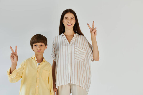 Улыбающаяся мать и ее сын выражают счастье, делая знаки мира своими пальцами..