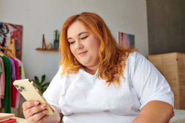 A plus size woman with vibrant hair engages with her smartphone, immersed in a relaxed atmosphere. clipart