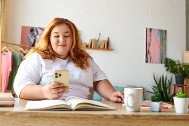 Büyük beden kadın, rahat bir kafede otururken telefonuyla konuşurken gülümsüyor..
