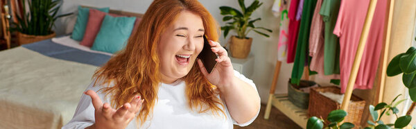 A beautiful plus size woman joyfully talks on the phone, surrounded by colorful clothes and plants.