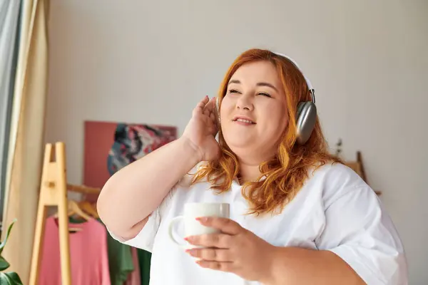 stock image A beautiful plus size woman relishes her favorite tunes while sipping coffee at home.