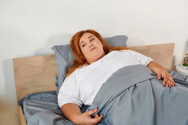 stock image A beautiful plus size woman enjoys a peaceful moment, comfortably resting in a cozy bed.