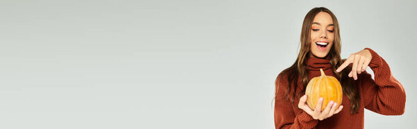 Красивая женщина наслаждается празднованием Хэллоуина, показывая свою тыкву с волнением.