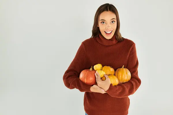 stock image A young woman in a comfy sweater joyfully holds pumpkins, embracing Halloween vibes.