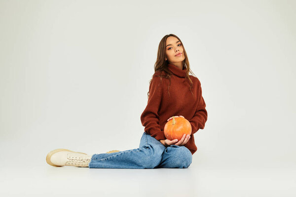Эта милая женщина надевает теплый свитер, сидя с тыквой, обнимая Хэллоуин вибрации.