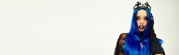 Молодая женщина показывает свой творческий костюм на Хэллоуин с смелыми голубыми волосами и короной.