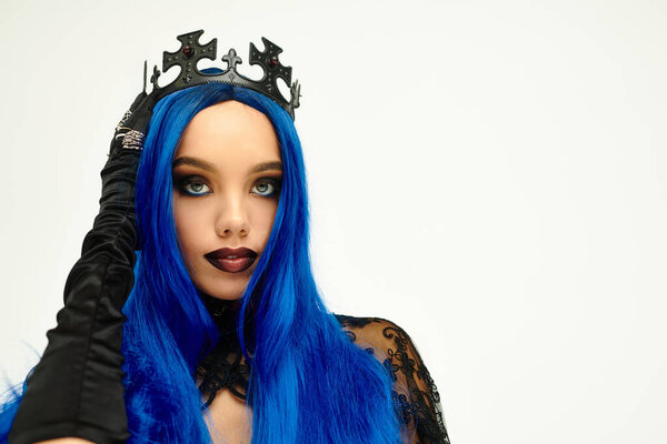 Одетые в драматический костюм на Хэллоуин, молодая женщина демонстрирует свои яркие голубые волосы и корону.