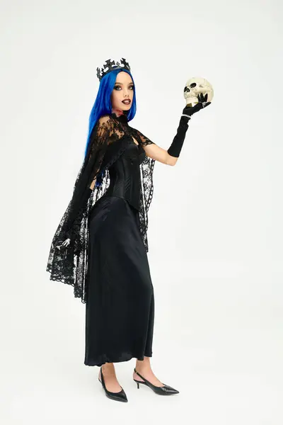 Stock image A young woman in an elegant black Halloween outfit holds a decorative skull, radiating mystery.