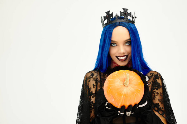 Красивая женщина, одетая в костюм на Хэллоуин, ярко улыбается, держа тыкву..