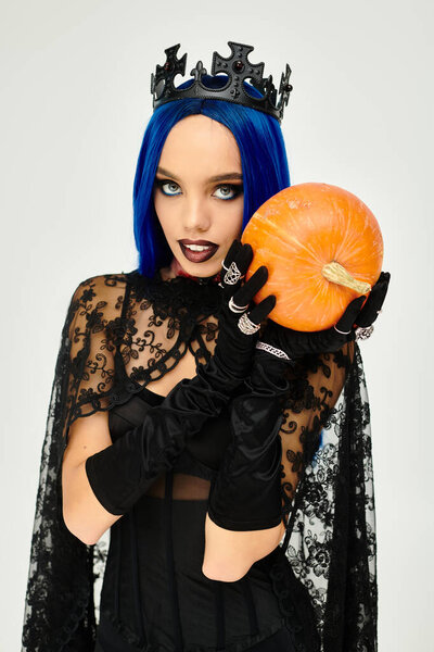 Молодая женщина в ярком костюме на Хэллоуин представляет яркую тыкву с очарованием.