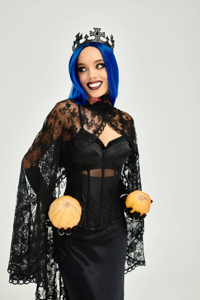 Красивая женщина в темном кружевном костюме привлекает внимание своими яркими голубыми волосами и тыквами.
