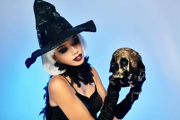 stock image A young witch gazes thoughtfully at a golden skull, embodying Halloween magic.