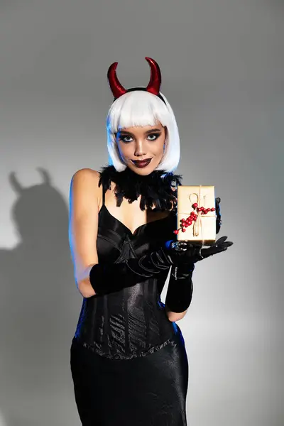 stock image The woman captivates with her devil inspired outfit and playful demeanor, holding a gift surprise.