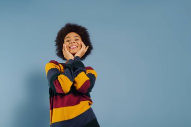 A cheerful young woman radiates happiness while playfully posing with her hands on her face. clipart