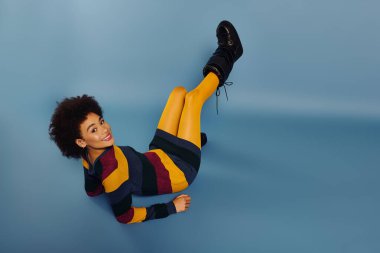 Genç bir kadın ışıl ışıl gülümser, canlı kıyafetini sergilerken sakin mavi bir arka plana karşı.