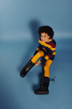 A young woman expresses joy while trying on oversized boots, showcasing her playful spirit. clipart