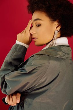 Genç bir kadın cesur bir arkaplana karşı düşünceli bir şekilde duruyor, derin duygularını ifade ediyor..