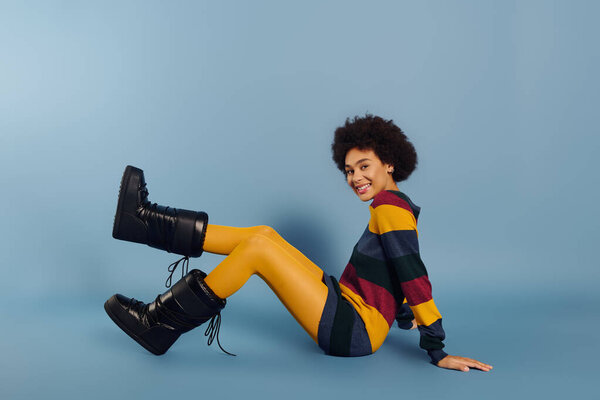 Молодая женщина показывает веселое выражение лица, сидя на полу в ярком одеянии.