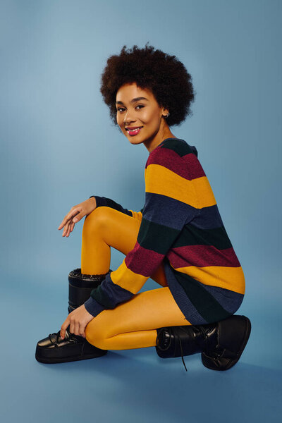 Молодая женщина с вьющимися волосами выражает эмоции, стильно позируя в яркой одежде..