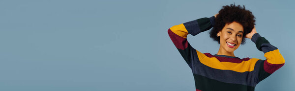 Молодая женщина с вьющимися волосами излучает счастье, играя в разноцветном свитере..