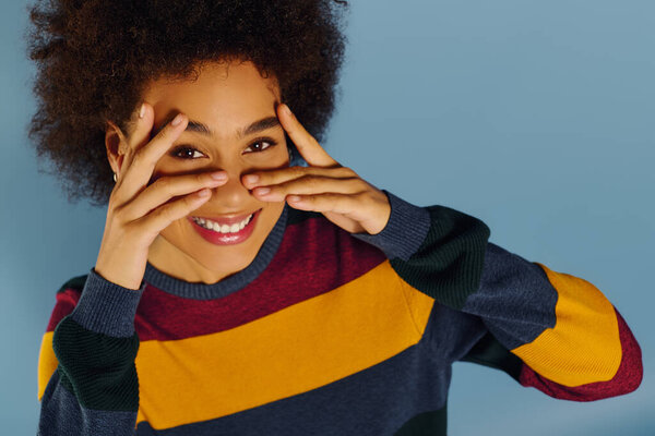 A young woman joyfully hides her face behind her hands, expressing playfulness and emotion.