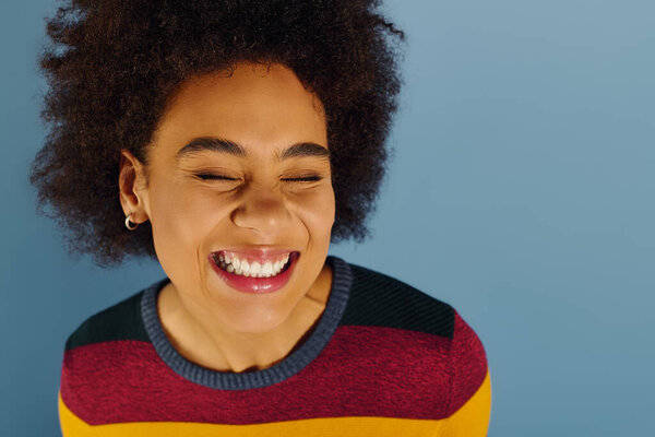 Молодая женщина с яркими кудрями лучами радости освещает мягкий синий фон.