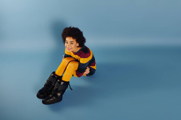 Молодая женщина с вьющимися волосами выражает счастье сидя на гладкой поверхности.