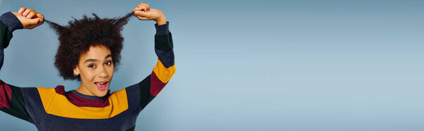 Молодая женщина с вьющимися волосами радостно тянет за волосы, демонстрируя свою яркую индивидуальность..