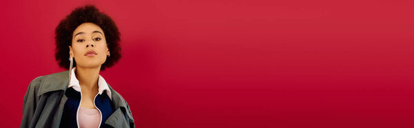 A young woman with an emotional expression stands against a bold red background, lost in thought.