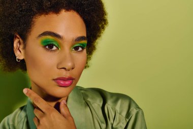 A young woman expresses emotion with striking green makeup, creating a captivating look. clipart