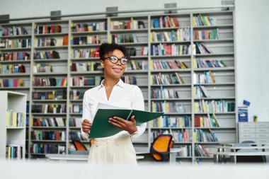 An enthusiastic teacher inspires students while standing confidently in a bright library. clipart