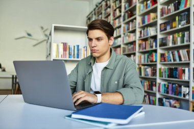 Çalışkan bir öğrenci kitap ve notlarla dolu bir kütüphane masasında çalışmalarına konsantre olur..