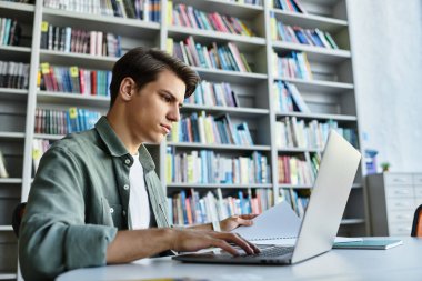 A focused student engages with his laptop while studying in a university library. clipart