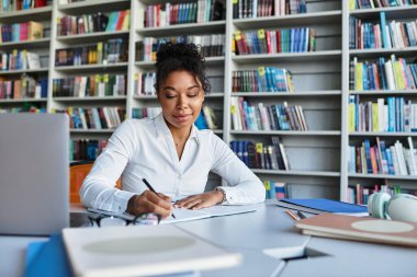 The teacher focuses intently on her lesson planning amid colorful bookshelves and supplies.