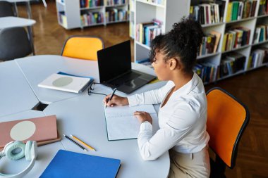 An inspiring teacher thoughtfully prepares lessons while seated at a dynamic library workspace.