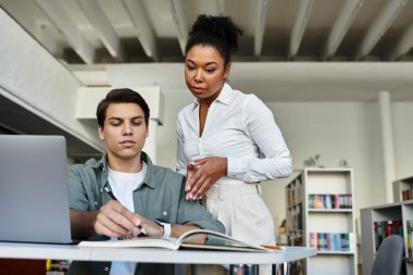 A student engages with a mentor in a library, examining materials for academic growth. clipart