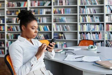 Kütüphanede telefonunu tutan tutkulu bir eğitimci..