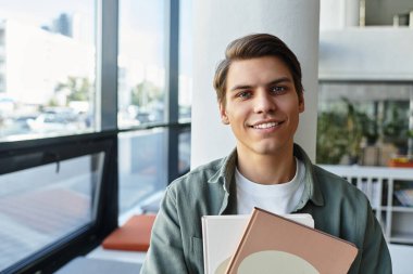 Cheerful handsome student in casual attire at school, studying hard. clipart