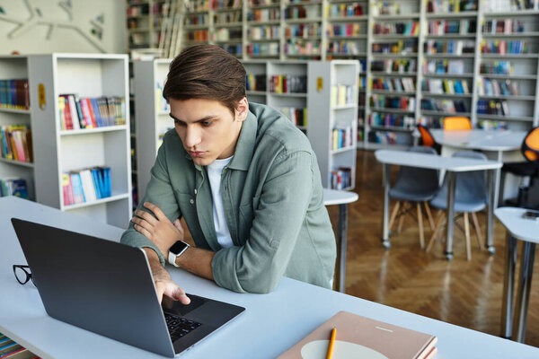 A dedicated young man engages in deep study at his laptop in a university library.