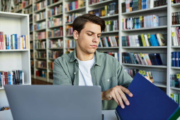 A focused young man diligently studies at a desk in a library, engaging with his materials.