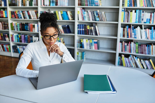 A dedicated African American teacher thoughtfully prepares lessons at her desk surrounded by books.