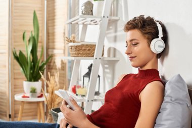 Kısa saçlı genç bir kadın evinde huzur içinde müzik dinliyor, günlük yaşamını kucaklıyor..