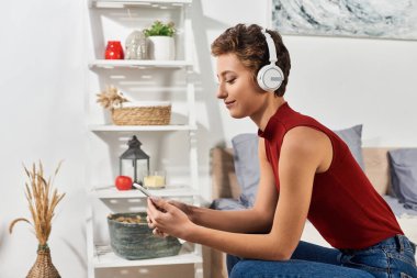 Genç bir kadın, günlük rutininin ve rahat atmosferinin tadını çıkarırken müziğe dalmış, evinde dinleniyor..