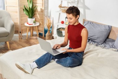 Genç bir kadın yatağında oturuyor, laptopuna odaklanmış, günlük rutininde samimi bir anı kucaklıyor..