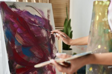 Genç bir kadın, rahat stüdyosunda renkli bir sanat eserini resmederken dikkatle odaklanıyor..