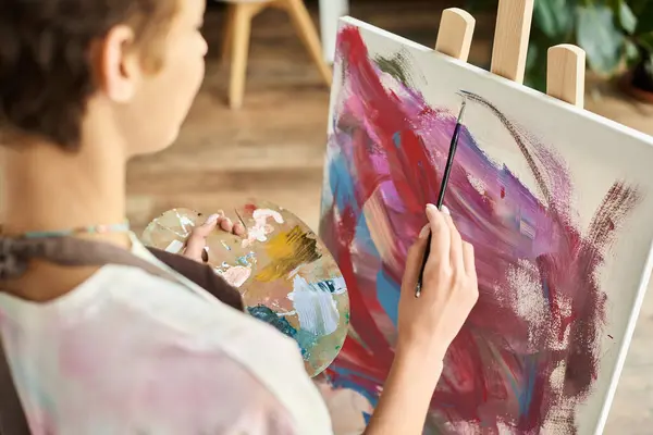 stock image A young woman in a relaxed setting focuses on painting with vibrant colors at home, expressing her creativity.