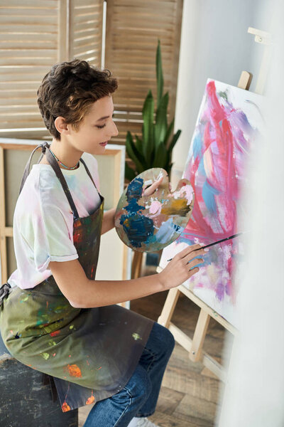 Молодая женщина с короткими волосами любит рисовать дома на холсте, выражая свою художественную страсть.