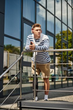 Genç bir adam, zorluklara rağmen hayatı kucaklarken korkuluklara yaslanır, müzik dinler..