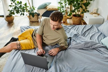Yakışıklı, genç bir birey, davet edildiği yatak odasından laptopuna dikkatle odaklanır..